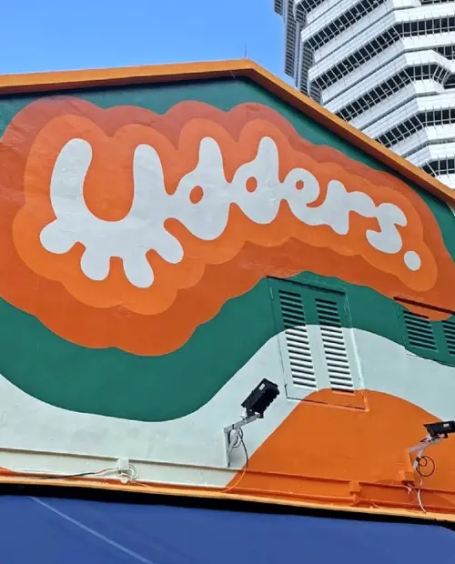 A bold orange and green mural with the Udders logo painted on the exterior wall of the ice cream shop at Beach Road, Singapore