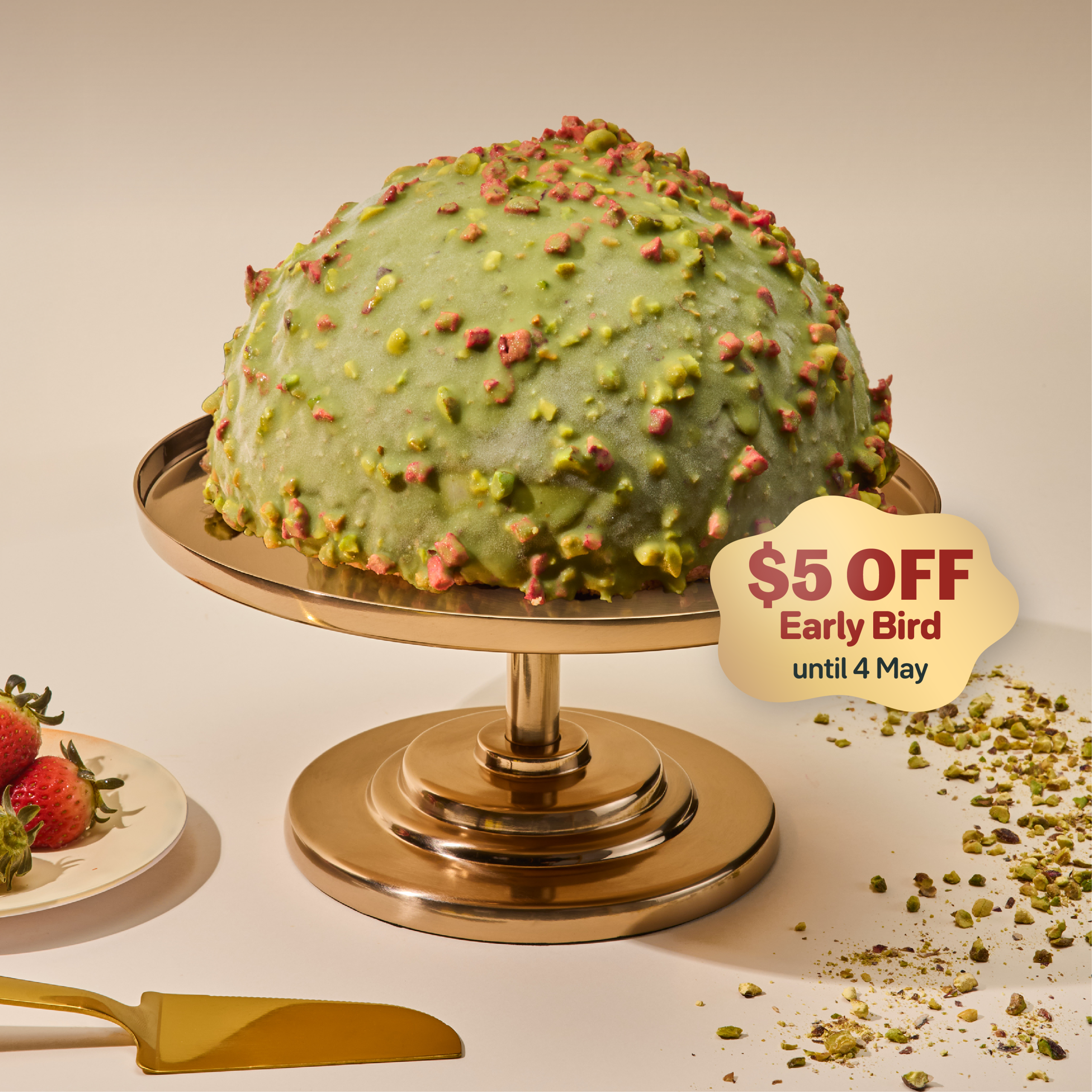 Pistachio blush dome cake covered in crushed pistachios and freeze-dried strawberries on a gold cake stand